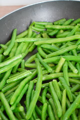 Close-up of fresh green beans being cooked in a non-stick frying pan for a healthy meal