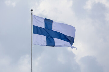 The Finnish flag flutters against a cloudy sky