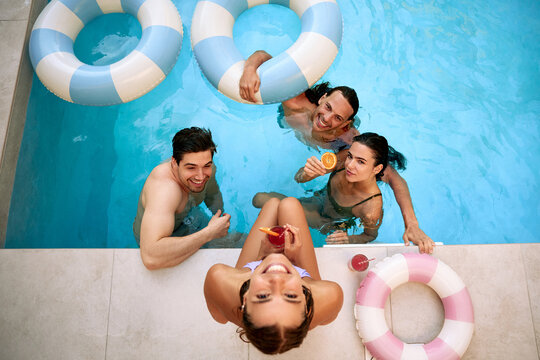 Happy friends enjoying drinks and relaxing together in pool during summer vacation
