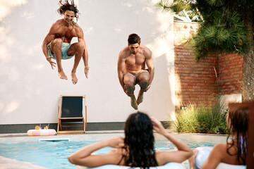 Men jumping into swimming pool while friends watch and enjoy summer vacation