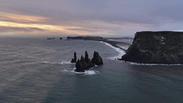 Aerial view of basalt sea stacks rising from the ocean near black sand Reynisfjara beach, with the sun rising in Iceland, Iceland.