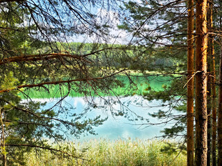 Lush forest framing a serene lake in the early afternoon sun, showcasing vibrant blue-green waters...