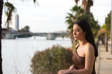 Portrait of a young, beautiful Spanish woman in a brown dress leaning on the railing, gazing...