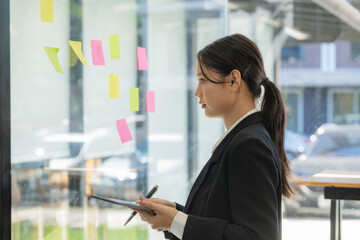 Fototapeta premium Confident businesswoman planning while looking at adhesive notes stuck on a glass wall.