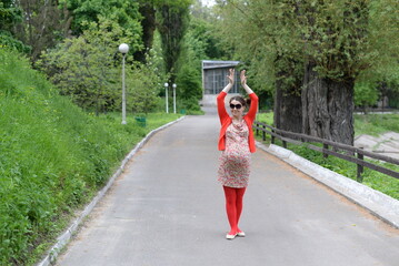 Pregnant girl in a dress and red blouse posing in the park