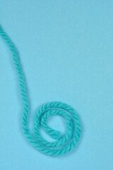 A thick, turquoise blue strand of yarn is neatly coiled into a spiral shape on a slightly darker, plain blue background with ample copy space