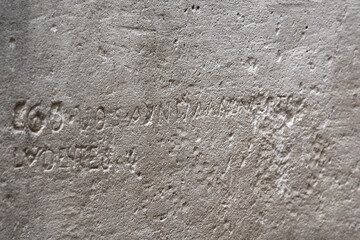 Close-up of a beige limestone wall. An ancient inscription, almost erased by time, is hidden on a central block, suggesting history and mystery.