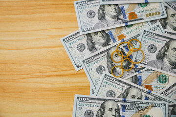 A pile of hundred-dollar bills arranged on a wooden surface. Several gold-colored keys are placed on top of the money