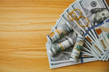A collection of U.S. dollar bills and rolled banknotes on a wooden surface. The scene emphasizes finance and currency