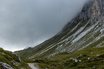 dettagli di un pendio erboso e roccioso di una montagna, col cielo coperto da nuvole basse e grigie, nelle Alpi del nord Italia, di giorno, in autunno