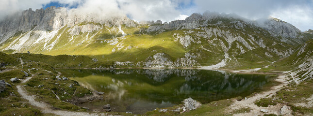 ampia composizione panoramica sui Laghi d'Olbe, circondati da catene montuose, in un ambiente naturale tra le montagne del Friuli Venezia Giulia, in Italia, con cielo nuvoloso, di giorno, in autunno