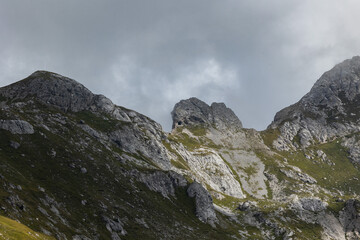 alte creste rocciose di una catena montuosa nelle Alpi del nord Italia, nella penombra, di giorno, con un cielo nuvoloso sullo sfondo