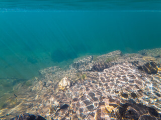 Serene underwater landscape of a pristine Norwegian lake, with beautiful sunlight creating caustic patterns on the rocky bed.