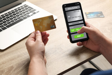 Man with credit card using smartphone for online payment at table, closeup
