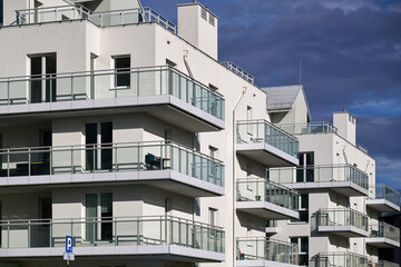 Modern white apartment balcony horizontal rows glass panel railing minimalist architecture facade detail blue sky sunlight Poland Gdansk residential property contemporary