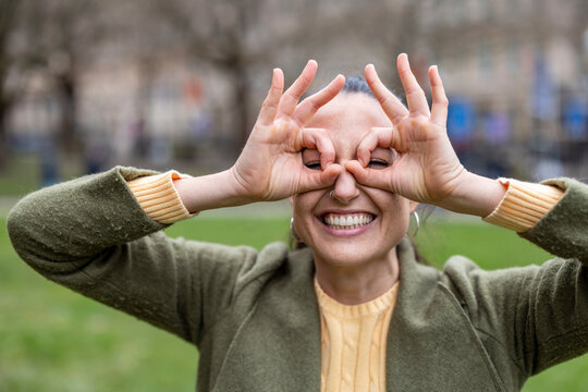 Playful portrait of smiling adult outdoors making hand gesture in park
