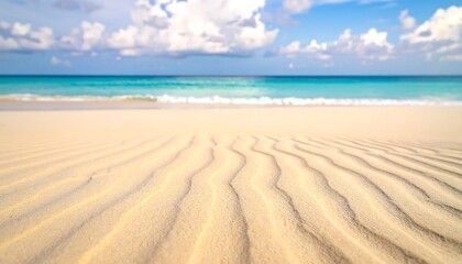 Obraz premium Bright, sun-drenched beach with waves in the sand and a clear turquoise sea under a cloudy sky