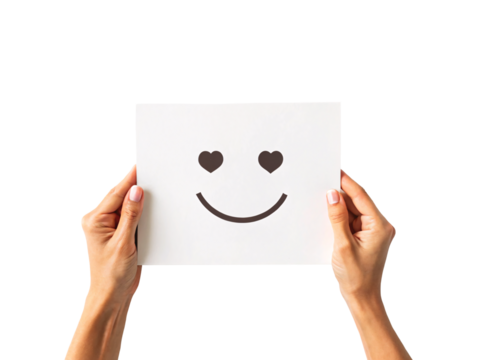 Hands holding white paper with smiley face featuring heart-shaped eyes and happy smile, isolated on a transparent background