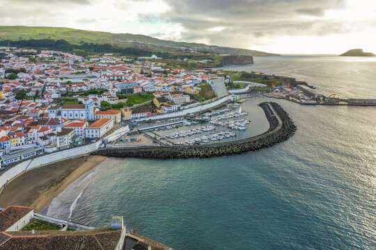 Aerial view of the vibrant town meeting the tranquil harbor, the red roofs contrasting the azure waters, a serene coastal scene, Angra do Hero&Atilde;&shy;smo, Azores, Portugal.