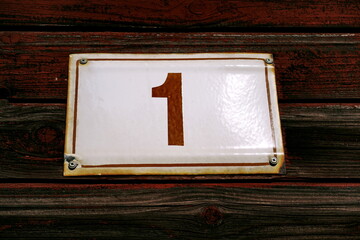 Numéro 1. Plaque de numéro de rue sur façade en bois peint en rouge.