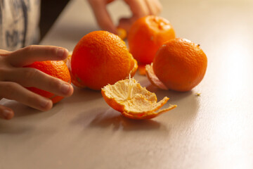 A small childs hands eagerly reach for vibrant oranges placed atop a table, which also features one peeled orange
