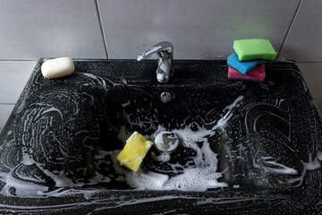 Modern black bathroom sink with chrome faucet, colorful sponges and soap.
Cleaning products quickly and effectively remove dirt and grease from the sink, ensuring perfect cleanliness.