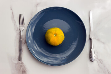 A conceptual image of a blue plate, fork and knife placed on a bright dining table. The concept: diet, food restriction, and mindful eating.