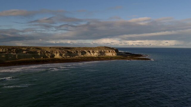 Aerial view from a drone gliding above the Atlantic Ocean, revealing coastal cliffs and wild surf in Patagonia, Argentina. Vast waters, isolated coastline, rugged natural landscape, South America.