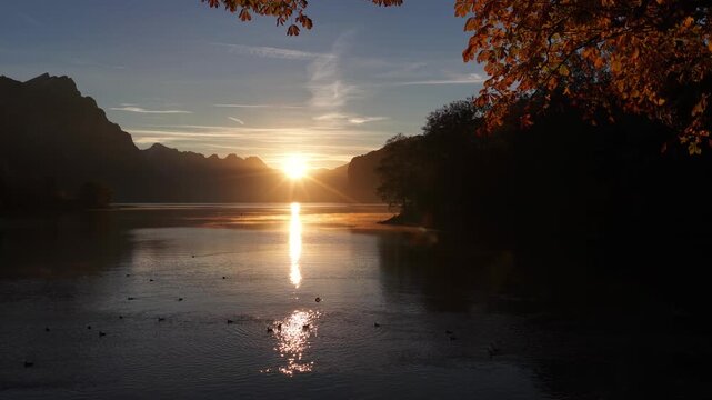Walensee lake at sunset in Walenstadt, Switzerland, aerial drone pulling back over, beautiful golden light, calm water and autumn trees.