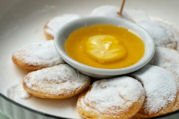 A plate of traditional Dutch mini pancakes (poffertjes) dusted with powdered sugar, served with a custard dip and a Dutch flag topper.	
