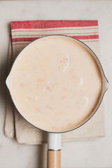 Homemade creamy cheese soup in a pot on a textile napkin, top view, rustic comfort food concept