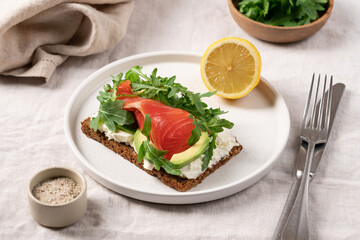Open sandwich on whole grain bread with smoked salmon, soft cheese, avocado and arugula, healthy gourmet breakfast