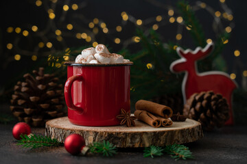 Hot chocolate with marshmallows in a red mug on a festive background with pine branches and cones for Christmas and winter holidays