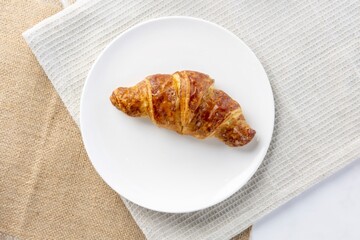 Golden croissant resting on white plate and linen
