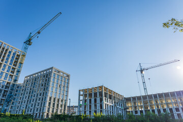 Fototapeta premium Builders are actively working on new residential structures at a construction site, with cranes and bright blue sky above