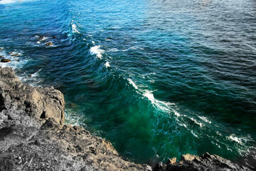 View from rocky cliff over turquoise ocean with long wave and foamy crest, scenic coastal landscape, dramatic seascape