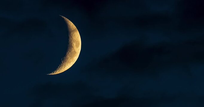 Waxing crescent moon slowly sinking behind dark clouds at night. Timelapse of the moon disappearing into the horizon, atmospheric night sky with dramatic shadows.