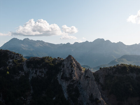 Aerial view of dramatic mountain peaks reaching for the sky, their rugged faces contrasting against the soft, ethereal clouds, Teth, Shkoder County, Albania.