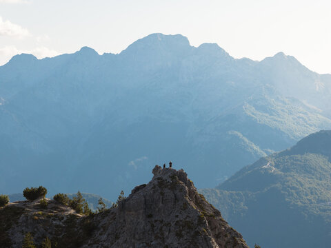 Aerial view of silhouetted figures atop a rugged peak with the majestic, hazy mountains, Teth, Shkoder County, Albania.