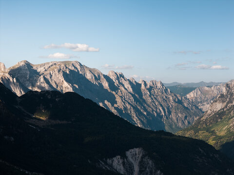 Aerial view of jagged, sun-kissed peaks casting deep shadows over verdant valleys, a serene dance of light and form unfolds in the Albanian Alps, Teth, Shkoder County, Albania.