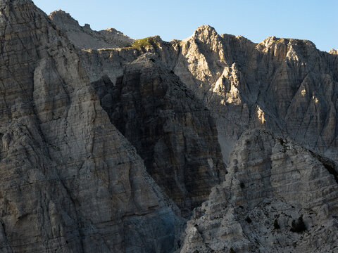 Aerial view of jagged, sun-kissed peaks casting deep shadows, creating a dramatic contrast of light and dark across the rugged landscape, Teth, Shkoder County, Albania.