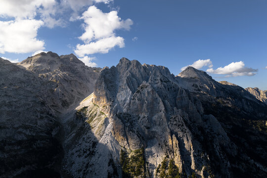Aerial view of sharp, rocky peaks rise towards the sky, their rugged faces contrasting with the soft, scattered clouds above, Teth, Shkoder County, Albania.