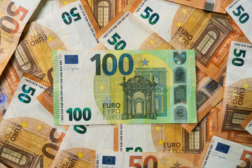 Closeup Top down flat lay of a 100 Euro banknote prominently centered on a background of stacked 50 Euro cash