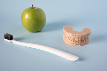 Toothbrush, green apple, and dental mold on blue background symbolizing oral hygiene, dental care, and healthy lifestyle choices.
