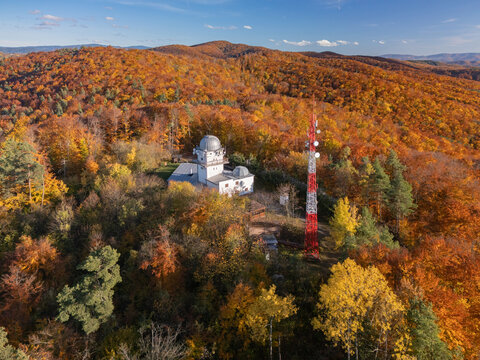 Aerial view of the Vartovka astronomical observatory stands amidst a sea of autumnal foliage, crowned by a crisp blue sky, Banska Bystrica, Banskobystricka kraj, Slovakia.