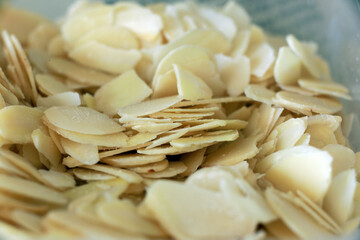 Close-up image of almond flakes in a wooden bowl on a dark textured background. High-quality food photography suitable for healthy eating, recipes, and nutrition themes.