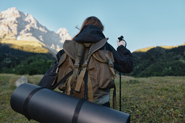 A lone adventurer wearing a sturdy backpack marches across a wide meadow toward looming mountains under a clear sky, preparing for a hike and outdoor exploration.