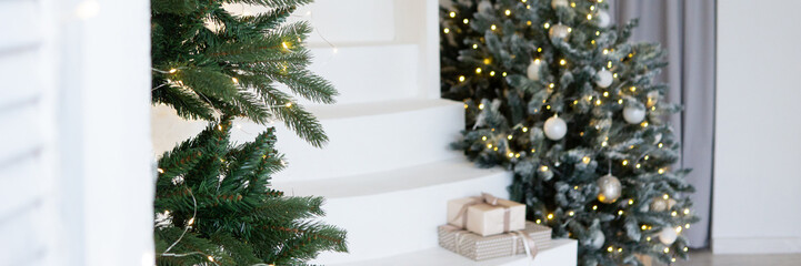 A large Christmas tree in the living room, decorated with garlands and light balloons. Bright Christmas interior with a white staircase.