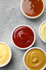 Different tasty sauces in bowls on grey table, flat lay