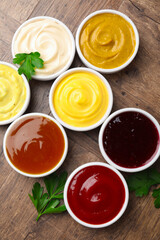 Different tasty sauces in bowls and parsley on wooden table, flat lay